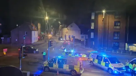 Contributed A wider view of the scene of a crash in a town centre where several emergency vehicles have parked at. Their emergency lights are on. Officers and paramedics in their uniforms and hi-vis are on the scene. 