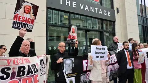 Pacemaker A number of people stand outside The Vantage office building on Belfast's Great Victoria Street. There are people holding up small signs saying 'Scrap the Legacy Act and ICRIR' and others saying 'Resign now' with an accompanying image of a judge.