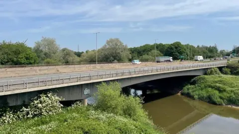 A view of the Over Bridge over the river Severn with light traffic on it. Underneath the water of the river, which is dark brown, can be seen flowing
