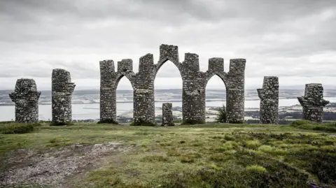 A large stone folly built overlooking a body of water.