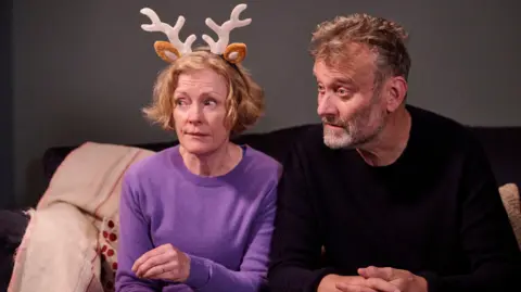 BBC/Hat Trick Productions/Adam Lawrence Kanan ke kiri: Claire Skinner memakai tanduk rusa, dan Hugh Dennis