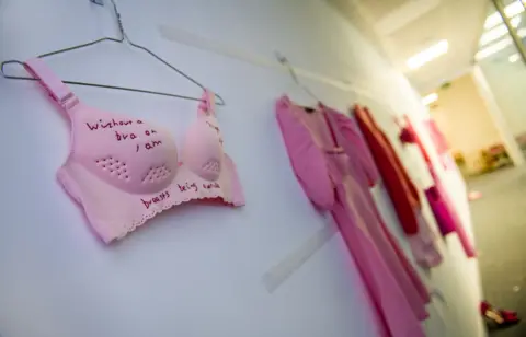 Embroidered clothing hang along a wall in a corridor of the perfromance space