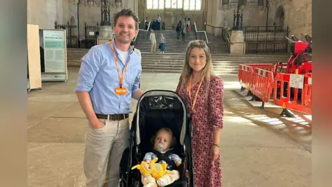 Harvie Strange Barney and Harvie Strange standing either side of the pram with Rafferty in it. They are inside the Houses of Parliament building.