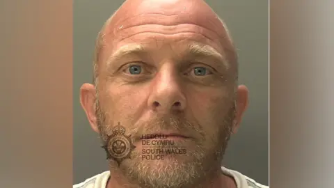 South Wales Police Geraint Boyce is a bald man with a grey and blond beard, blue eyes and blond eyebrows. There is a watermark reading South Wales Police across his mouth