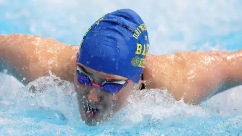 Getty Images A swimmer is swimming towards the camera in a blue cap and goggles.