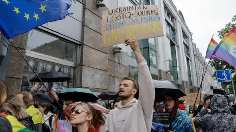 EPA/Sergey Dolzhenko People at Pride march including a man holding a sign saying "Ukrainian LGBTQ soldiers defend our freedom - give them their rights"
