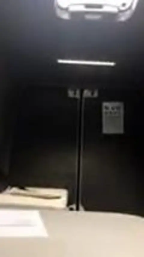 Swansea Trading Standards A grainy image of the interior of a van with a skylight in the roof. Short dark grey carpet covers the internal walls and doors and a small white poster, featuring letters for an eye test hangs on the back wall. 