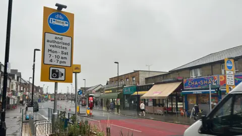 LDRS A view of the traffic-restricted zone on Portswood Road in Southampton. A red block of colour is seen on the road indicating the start point of the restricted zone and a sign detailing the restrictions is on the left hand side. Shops are visible on the opposite side of the road.