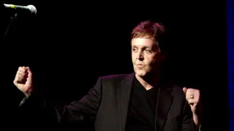 PA Media Sir Paul McCartney punches the air after singing on stage at the Empire Theatre in 2002