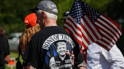 REUTERS/Eduardo Munoz A man stands with his back to the camera holding an American flag while wearing a Trump T-shirt.