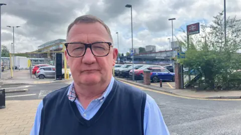 Photograph of Richard Slater from Henbury Travel. He is pictured in front of the railway station in Macclesfield town centre.