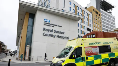 Reuters A yellow and green ambulance parked in front of a large white building, with a sign on the building saying Royal Sussex County Hospital