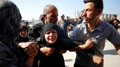 A woman wearing black clothing looks distressed as she's helped by people around her