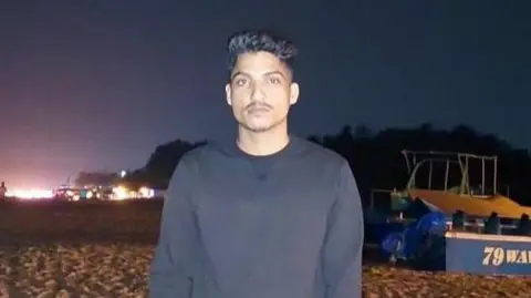 Satish Rana, from Uttarakhand, standing on a beach, wearing a black full sleeve pullover