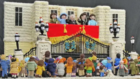 A knitted scene of the Royal family waving from Buckingham Palace at a crowd.