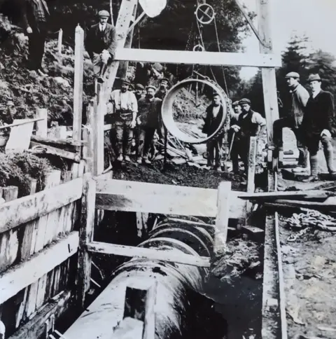 Severn Trent Several workers, pictured in black and white, stood around a wooden contraption with a suspended hollow circle.