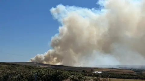 Simon Torr Thick grey smoke is seen blowing over fields from a distance