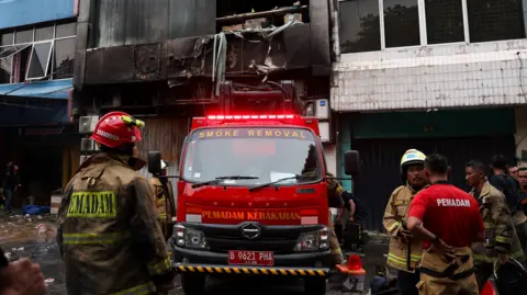 Reuters Firefighters stand near a seven-storey building damaged by fire, in Jakarta, Indonesia, 9 December 2025