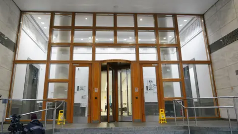PA Image of entryway to Parole Board offices. It is a large entrance with stairs leading up to it. The wood panelled doors are surrounded by lots of windows. 