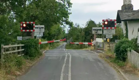 Google Maps Cross Lane leading to the level crossing. The barriers are down. 