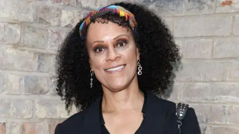 Bernardine Evaristo, wearing a black top, a headband and dangly earrings.
