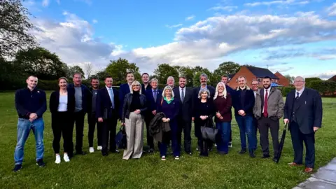 Reform UK A group of men and women stand in a field.