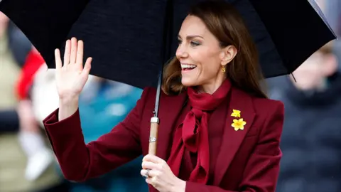 Getty Images Princess Catherine waves to the crowd wearing a burgundy suit with a daffodil on the lapel