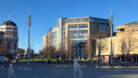 A large eight-floor office building with big glass windows viewed from Bradford's City Park.