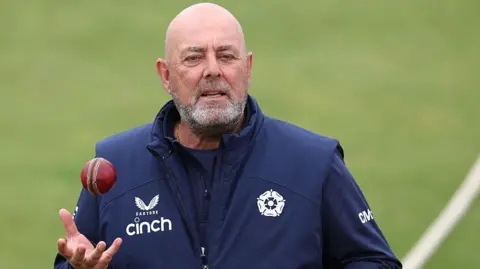 Darren Lehmann standing on a cricket pitch holding his right hand out ready to catch a cricket ball