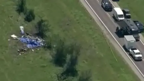 A view of the crash site on the left with vehicles parked along the road to the right