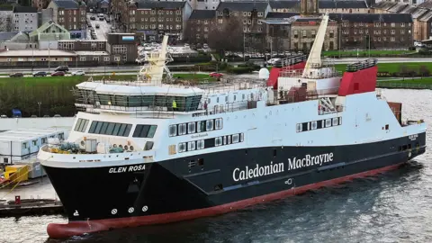 A large ferry moored at a quayside. Caledonian MacBrayne is written on the side with the name Glen Rosa at the front. The ship is black and white with red funnels