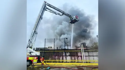 An aerial arm over lots of smoke with a hose firing water below