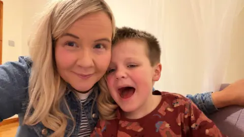 Fiona Forrest Fiona and Ted are posing for a selfie. She has blond hair and she's wearing a stripped top and a denim jacket. Ted has brown hair. He's wearing a top decorated with bears. 