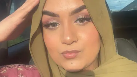 Selfie picture of Nimra, looking at the camera. She is wearing a green hijab and has a nose ring.