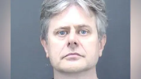 Dorset Police A mug shot of a man with medium-length grey/white hair.