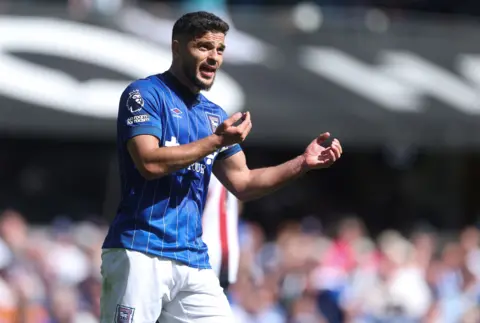 Ipswich Town's Sam Morsy has dark hair, and a beard. He is wearing the blue and white Ipswich kit, and is gesturing to a teammate with instructions. 