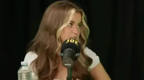 PoliticsJoe Laura Beveridge at a microphone. She has long brown hair and is looking to the right, as if talking to someone. The microphone has the word "JOE" written on it.