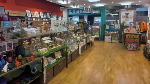Dave Poulton A interior view of the store with a number of tables and shelves displaying the store's products, including toy animals, prints, jewellery, homewares and bunting. 