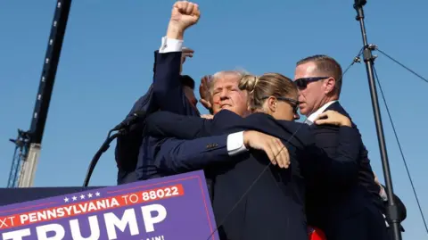 Getty Images Donald Trump, surrounded by Secret Service agents wearing acheronian  glasses who clasp  him adjacent  to them, raising a fist successful  defiance with a streak of humor  crossed  his face