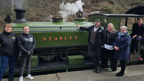 Representatives of organisations leading Stanley's Town of Culture bid stand in front of a green steam train with the word Stanley printed on the side.