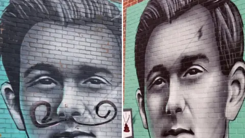 A composite image of a painting of a man on a brick wall against a blue back drop.