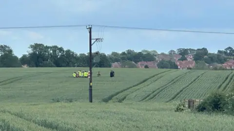 James Hill Emergency workers can be seen in a field where an aircraft has crashed.