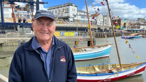 Paul Arro. Behind him is Bridlington harbour, which contains two cobles.