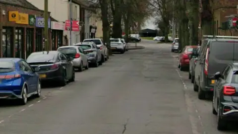 Queen Street in Brigg. There are cars parked on either side of the road, along with a number of shops and businesses.