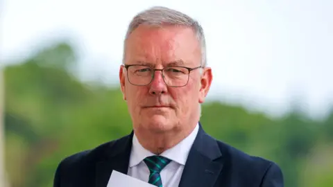 PA Media Mike Nesbitt, a man with a white shirt, green striped tie and blue jacket. He has grey hair and is wearing glasses.