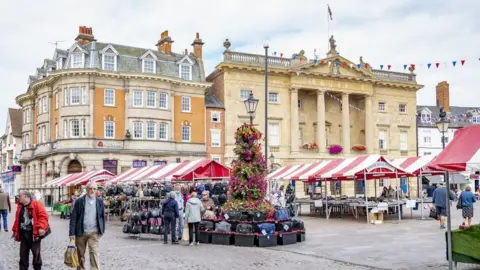 A ground level view of Newark market square, with a number of stalls set out and shoppers moving around