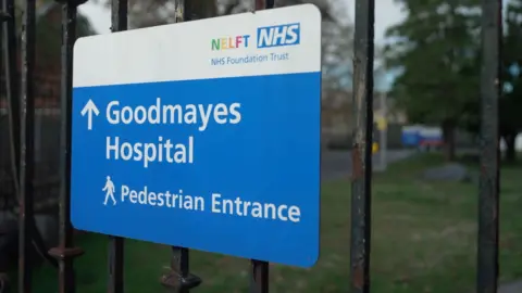 Blue sign on an iron railing, saying Goodmayes Hospital Pedestrian Entrance
