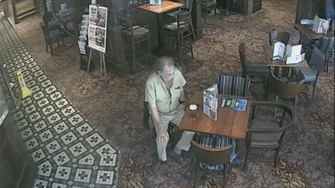 Crown Prosecution Service A CCTV still image of a man sitting in a pub with a full pint of beer on his table. 