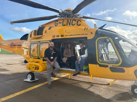 Lincs and Notts Air Ambulance Andy Wilkins is pictured with two members of the team from the Lincs & Notts Air Ambulance. They are perched inside the yellow air ambulance helicopter. 