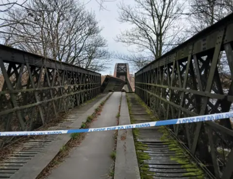 Roddy Robertson A bridge with the central section collapsed and police do not cross tape in the foreground